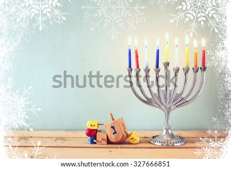 image of jewish holiday Hanukkah with menorah (traditional Candelabra) and wooden dreidels (spinning top). glitter and snowflakes overlay
