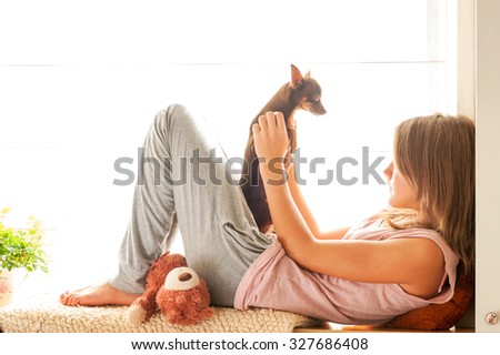 Good Morning! Teenage girl in pyjamas holding her small brown toy-terrier dog. Vibrant multicolored horizontal image.