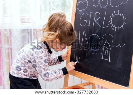 Little beautiful girl drawing on a blackboard. Learning at Home.