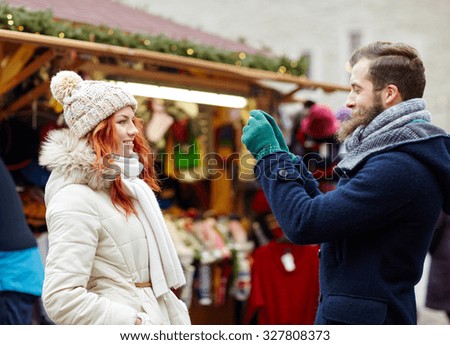 holidays, winter, christmas, technology and people concept - happy couple of tourists in warm clothes taking picture by smartphone or camera in old town