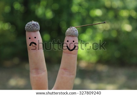 In the picture two fingers in hats on acorns. At the toes painted smile. nature. In the background of green trees. 
