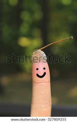 One finger on the picture of an acorn hat. On finger painted smiley smile. nature. In the background of green trees. 