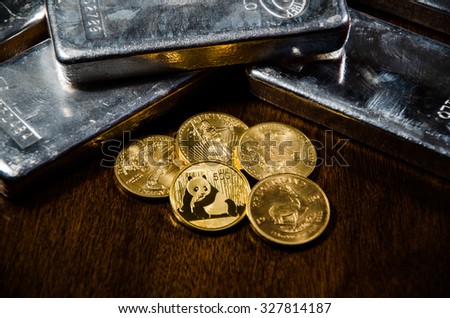 These Gold coins & Silver bars produce vivid reflections & shadows on a wooden table. Royalty-Free Stock Photo #327814187