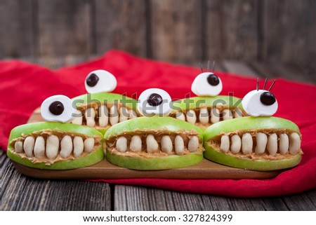Cute scary halloween apple cyclop monsters food healthy vegetarian celebration party snack dessert recipe with red fabric on vintage wooden background. Edible funny decoration 