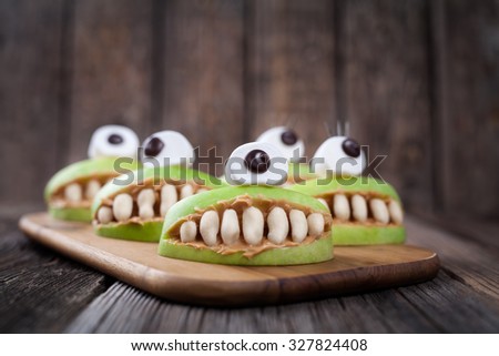 Scary halloween edible apple monsters healthy natural dessert. Horror party for kids decoration delicious snack. Homemade cute cyclop mouth with teeth and peanut butter on vintage wooden table