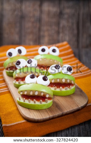 Homemade scary halloween edible monsters for celebration eve party decoration. Natural healthy sweets food recipe. Cute apples mouth with eyes, sunflower seeds and jam on vintage wooden background. 