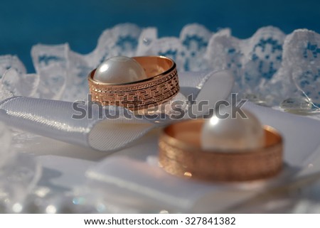 Closeup of two beautiful luxury golden engagement rings lying together on soft white fabric with lace and pearl beads on wedding celebration indoor, horizontal picture