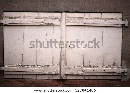 Closeup outdoor locked retro old timber wooden painted white peeling window shutters against grey concrete facade wall background for privacy and defence, horizontal picture