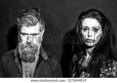Closeup view of couple of painted halloween holy chracters woman and man with long lush beard looking forward on studio wall background black and white, horizontal picture