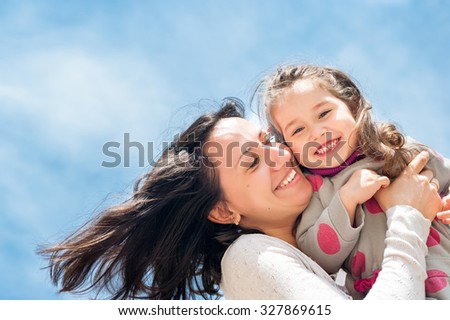 Happy mother and daughter look in the camera and laugh. The picture is photographed from below, the bright blue sky as a background.