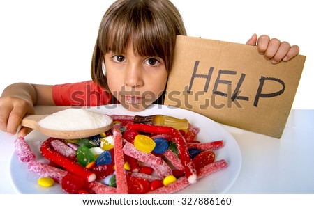 sad and vulnerable 4 or 5 years old female child asking for help  eating dish full of candy holding sugar spoon in sweet abuse dangerous diet and unhealthy nutrition concept isolated on white Royalty-Free Stock Photo #327886160