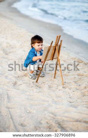 A child on the beach draws by paint on the easel on the beach