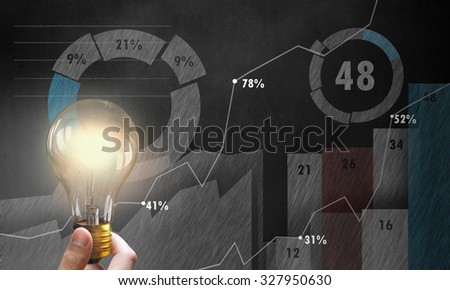 Male hand holding light bulb on background of diagrams and graphs
