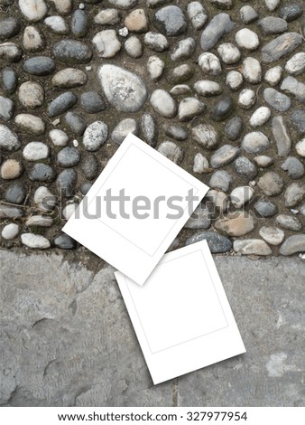 Two square instant photo frames on pebble and concrete street background