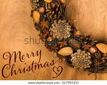 Merry Christmas message, handmade natural wreath decoration pine cones, almonds, anise stars and hazelnuts over wooden background - retro style design