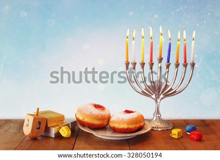 image of jewish holiday Hanukkah with menorah (traditional Candelabra), donuts and wooden dreidels (spinning top). glitter overlay
