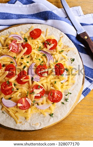 Flat tortilla with cheese and vegetables on wooden surface