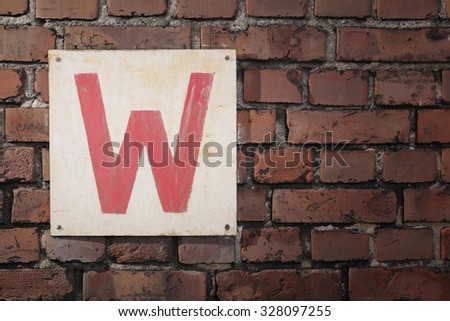 Old sign with letter W on a brick wall.