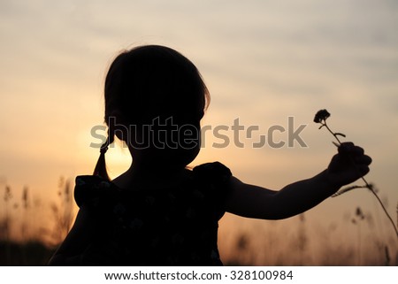 Silhouette of a little girl picking flowers on meadow, at sunset