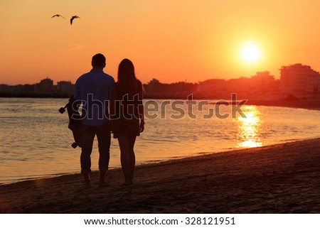 Silhouette of happy couple standing near the sea and take a photo during sunset. Girlfriend and boyfriend during romantic date moment. Love concept of peace or quiet vacation for loving hearts.