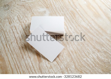 Photo of blank business cards with soft shadows on light wooden textured background. For design presentations and portfolios.
