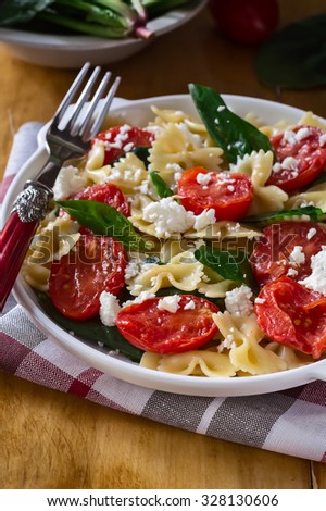 Farfalle pasta with Tomatoes, Spinach and Cheese in a plate on a wooden table