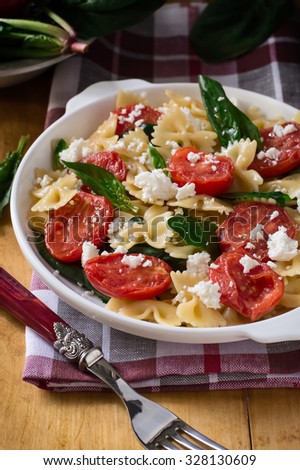 Farfalle pasta with Tomatoes, Spinach and Cheese in a plate on a wooden table