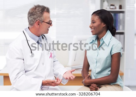 Pink awareness ribbon against doctor speaking with cheerful young patient Royalty-Free Stock Photo #328206704