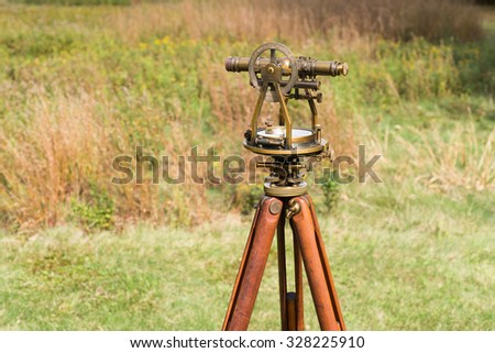 Vintage Surveyor's Level (Transit, Theodolite) with wooden Tripod in a field.
