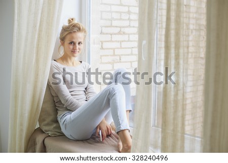 Blonde woman sitting on a window-sill and holding her smartphone