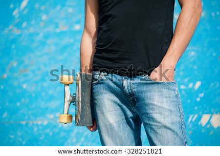 Detail of man holding skateboard at skatepark.
