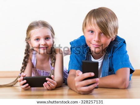 Smiling little girl and teenage boy burying in mobile phones laying on the floor. Focus on girl
 Royalty-Free Stock Photo #328257131
