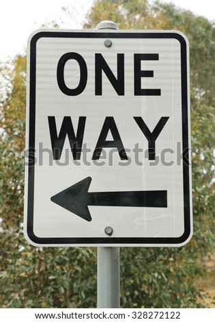 black and white one way sign against a tree background