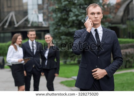Business confidence. Portrait of motivated businessman. Leader is working in business suit. Outdoors business concept. His business partners and colleagues are on the background