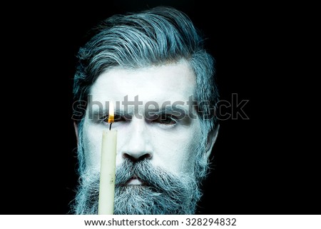 Portrait closeup view of one halloween holiday celebration character senior man with spooky painted face of zombi and long white lush beard holding burning candle black and white, horizontal picture