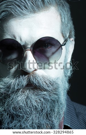 Portrait closeup view of one halloween holiday celebration character senior man with spooky painted face of zombi and long lush beard in sun glasses black and white, vertical picture