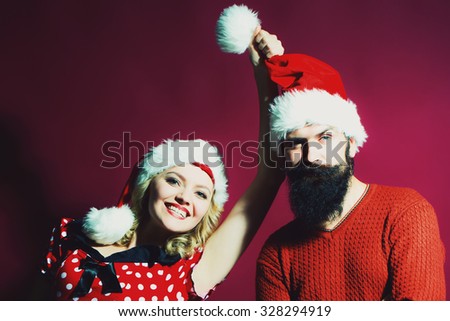 New year funny couple of blond woman with curly hair and man with long beard in red santa claus hat celebrating christmas standing on studio purple background, horizontal picture