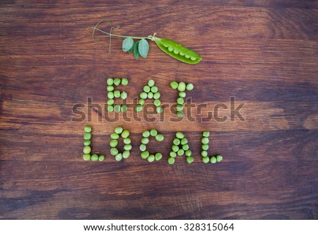 Sign "Eat Local" made of green peas and pea pod with leaves on wooden background. Organic vegetable produce at a farm.