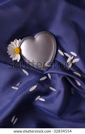 Silver heart on a sheet of blue satin carelessly draped