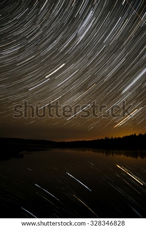 The picturesque night view of the lake, forest and stars in the form of tracks, reflecting in the water
