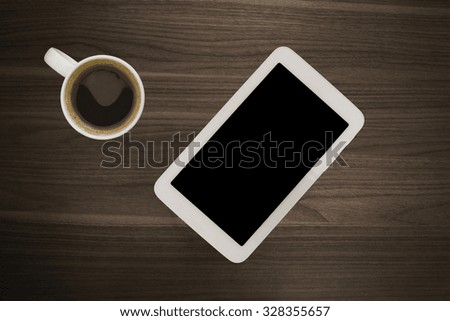 Digital tablet computer or smartphone phone with cup of fresh coffee on wooden desk. Simple workspace or coffee break with web surfing. Vignette light effect. or of free spare copyspace for content