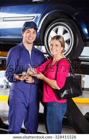 Portrait of happy mechanic with female customer while signing invoice in garage