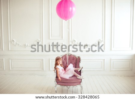 Kid girl 4-5 year old sitting in armchair holding pink balloon in room over white background. Looking at camera. Childhood. Cute little princess.  Royalty-Free Stock Photo #328428065