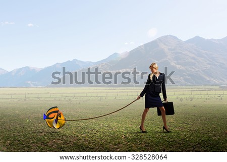 Young businesswoman walking with big exotic fish on lead