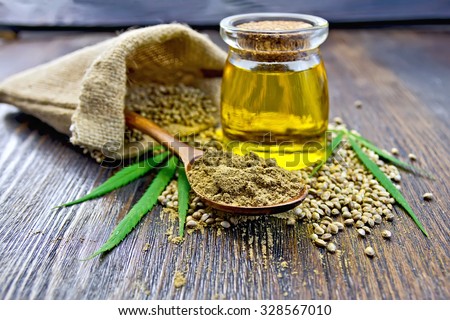 Flour hemp in a wooden spoon, seed in a bag and on the table, oil in a glass jar, cannabis leaves on the background of wooden boards Royalty-Free Stock Photo #328567010