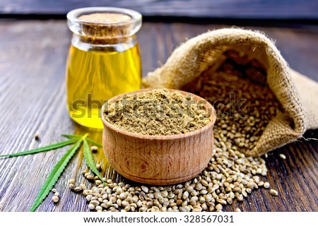 Hemp Flour in a wooden bowl, seed in a bag and on the table, oil in a glass jar, cannabis leaf on the background of wooden boards Royalty-Free Stock Photo #328567031