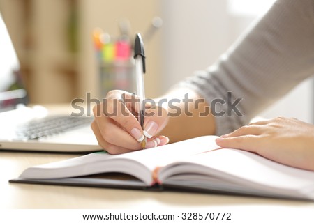 Close up of a woman hand writing in an agenda on a desk at home or office Royalty-Free Stock Photo #328570772