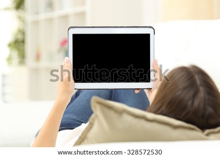 Woman using a tablet and showing a blank screen lying on a couch at home