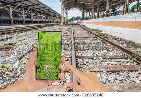 male hand is holding a modern touch screen phone and image of Railway lines travel through a railway station.(travel to nature concept)