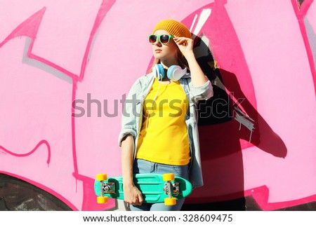 Fashion pretty cool girl wearing a yellow colorful clothes, sunglasses, headphones and skateboard in city